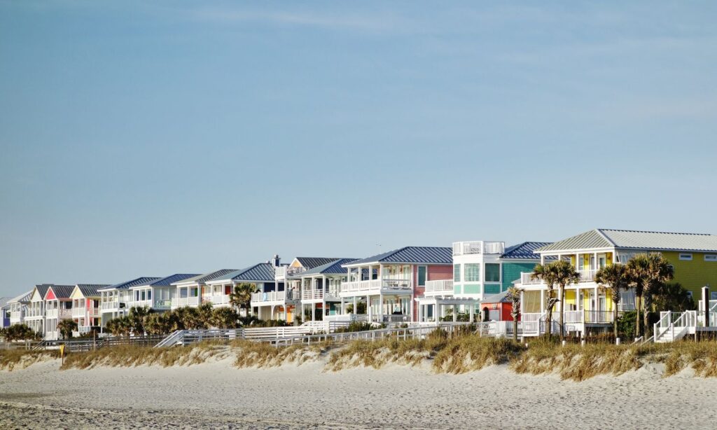 Colorful beach houses along the shore with palm trees and clear sky in Carolina Beach, NC.