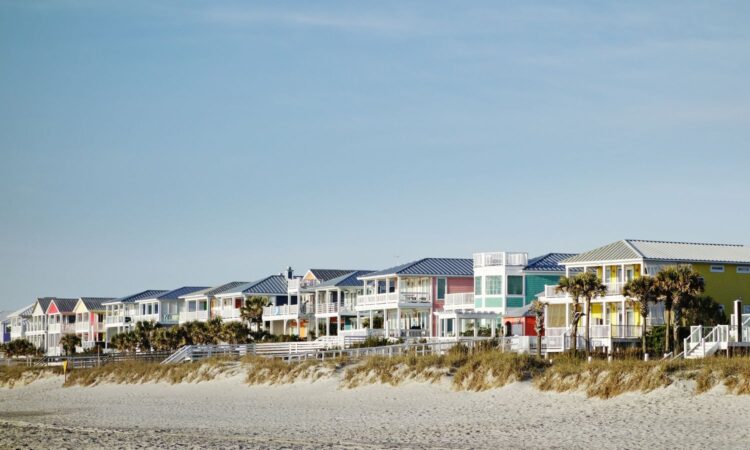 Colorful beach houses along the shore with palm trees and clear sky in Carolina Beach, NC.