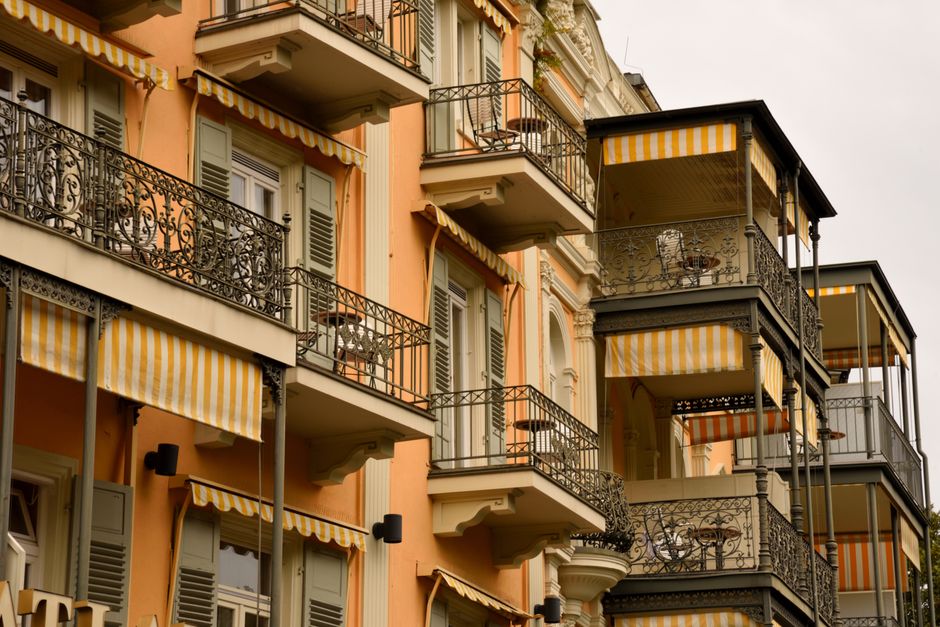 Sun-drenched iron lace balcony in New Orleans' French Quarter, adorned with lush green hanging plants and ferns, evoking t...